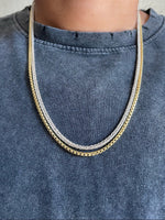 Load image into Gallery viewer, A close-up of a person wearing a double-strand chain necklace with one gold-toned chain and one silver-toned chain, styled over a faded blue-gray t-shirt.
